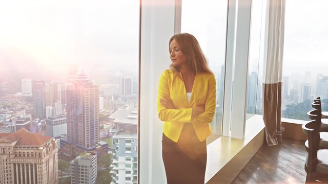 Young beautiful business woman staying by the window at modern building. Female modal looking in the city through window