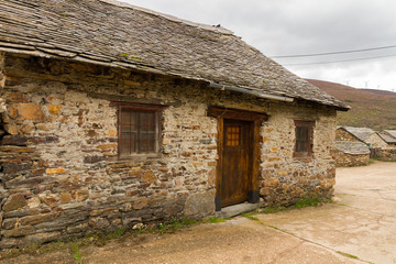 Fototapeta na wymiar Casita Tradicional de Piedra - Pequeña casa antigua y tradicional construida en piedra, puerta y ventanas de madera y el tejado con lajas de pizarra