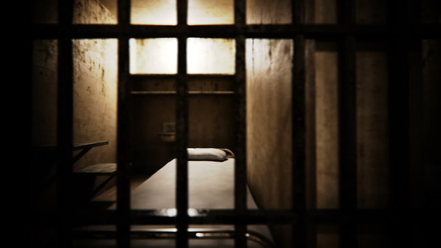 Empty prison cell interior seen through metal bars in dim light