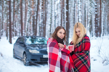 two girls sheltered red plaid hold mugs a drink in a snowy forest
