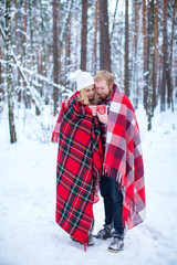 young couple sheltered red plaid holding a hot tea in winter wood