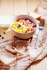 
Russian salad with potatoes , sausage , carrot , egg and green peas , mayonnaise or sour cream and spices on a wooden background