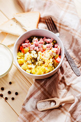 
Russian salad with potatoes , sausage , carrot , egg and green peas , mayonnaise or sour cream and spices on a wooden background