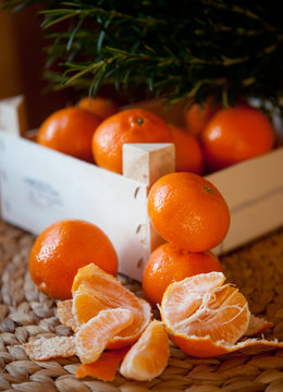 Ripe Mandarin fruit peeled open and place on old rustic look timber with group of mandarin fruits and leaves out of focus on the background 