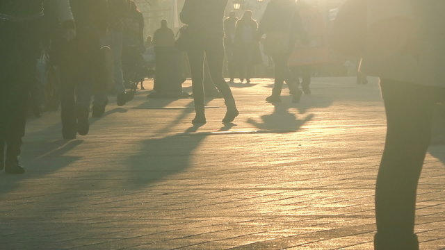 Unrecognizable group of people as street crowd walking the city streets in sunset, silhouettes of people and shadows on pavement.