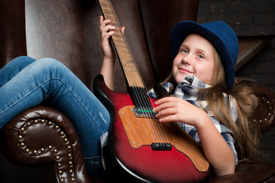 Little girl in hat playing guitar 