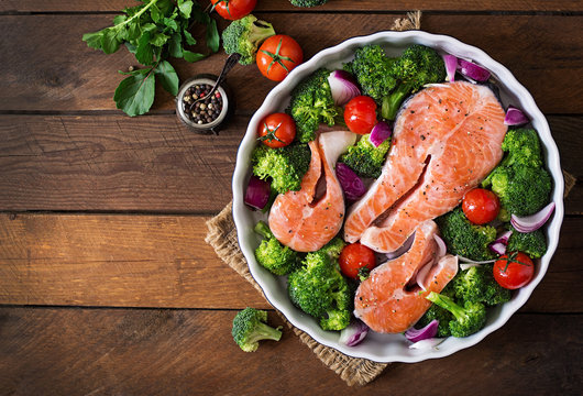 Raw salmon steak and vegetables for cooking on a dark wooden background in a rustic style. Top view