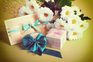 a bouquet of white daisies with a gift and envelope on wooden table,photo in the filter