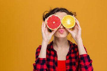 Funny playful woman holding halves of citrus fruits against eyes