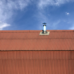 Naklejka premium Gable roof of a house covered with metal tile with short smokestack closeup against blue sky with white clouds