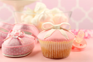 Fototapeta na wymiar Tasty cupcake with bow and baby shoes, pacifier on color background