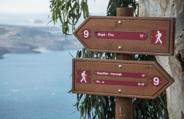 Signs along hiking path in Fira on the island of Santorini, Greece with the Aegean Sea in the...
