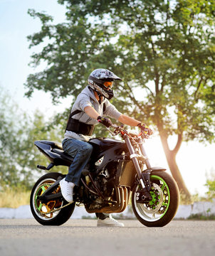 Dawn ride. Vertical shot of a stuntman posing on his motorbike in the evening sunlight on the road