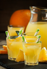 Orange drink in small glasses with striped straws and pitcher, s
