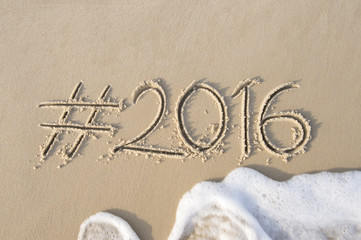 Hashtag social media message for 2016 written in smooth sand with incoming wave on the beach in Rio de Janeiro, Brazil