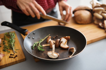 Closeup of mushrooms in a frying pan with woman slicing