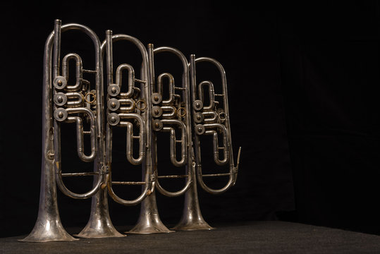 Four old brass wind instrument stand on a table