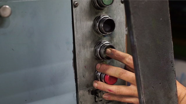 Close up handheld shot of a person's hand and finger hovering over an industrial machine button controller and turning the machine on and off by pushing the button and holding it.