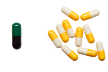 Pile of yellow and white capsules and one bigger green and black capsule isolated on white background. Clipping path included.