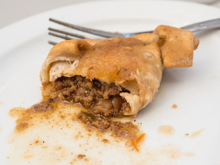 Half eaten empanada on a white plate with a fork hidden behind