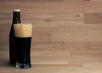 Stout beer in glass and bottle over wood