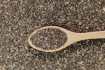 Handful of chia seeds on wood spoon and background