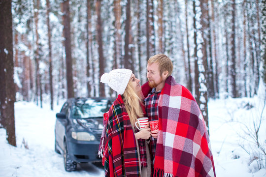 Young Couple Sheltered Red Plaid Holding A Hot Tea To The Car In Winter Wood