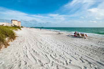 Beach against blue cloudy sky with relaxing people on sunchairs. Luxury holiday resort in Florida USA with white sand and azure water on a sunny day in summer