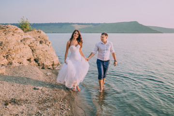 Fototapeta na wymiar beautiful gorgeous bride and stylish groom holding hands, on the background of a sea