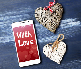 White smart phone with hearts on wooden desk.