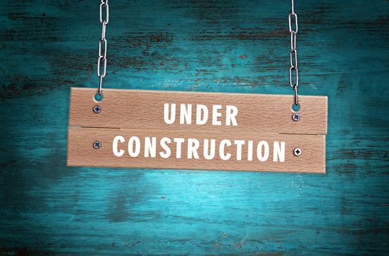 Wooden signboard with text Under Construction on wooden wall background