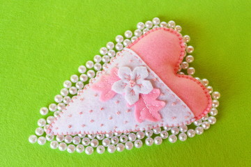 Hand-stitched felt heart - symbol of Valentines Day, on green background 