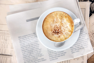 Cup of tasty cappuccino and newspapers on table
