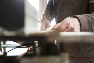 Carpenter cutting a piece with electric circular saw over table