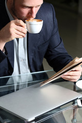 Young attractive businessman having lunch and working in a cafe