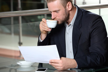 Young attractive businessman having lunch and working in a cafe