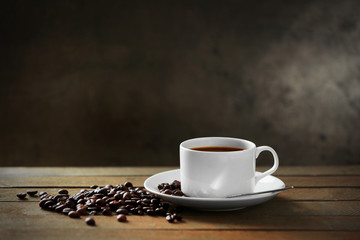 Cup of coffee and coffee grains on wooden table, on gray background