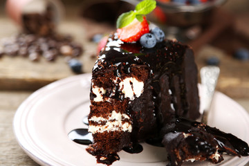 Chocolate cake with cream and fresh berries on plate, on wooden background