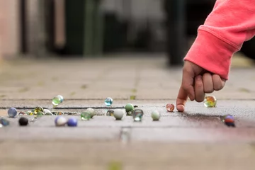 Child playing with marbles on yhe sidewalk.  old-fashioned toys still in use today. © mslok