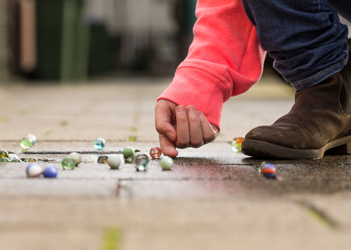 Child playing with marbles on yhe sidewalk.
old-fashioned toys still in use today.