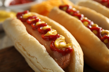 Tasty hot-dogs with French chips, spices and vegetables on wooden background, close up