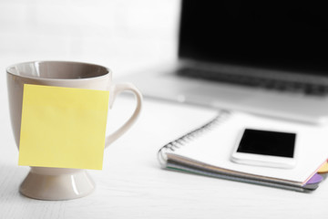 Yellow adhesive note on coffee cup, on laptop background