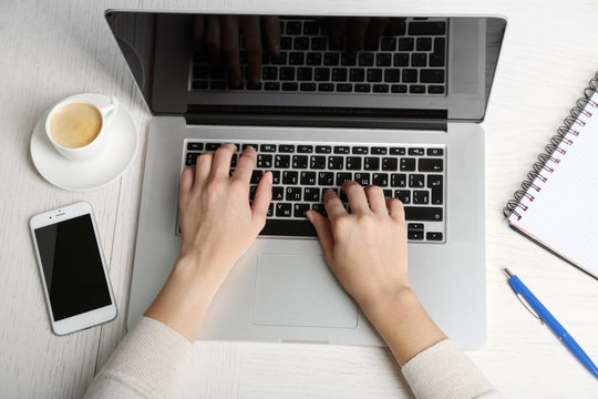 Woman working with laptop placed on wooden desk. Top view