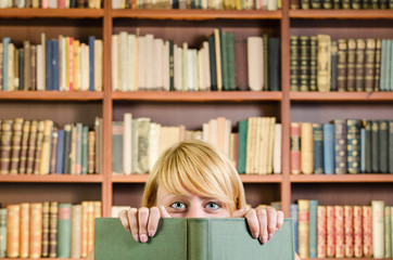 Blonde girl in library hiding behind a book