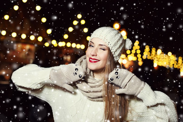 Portrait of smiling cheerful beautiful young woman on the festive Christmas fair. Funny posing. Lady wearing classic stylish winter knitted clothes. Magic snowfall effect. Close up
