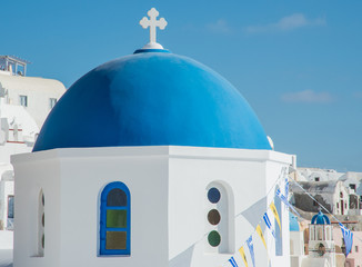 A Greek Orthodox church with blue and yellow prayer flags in Oia town on the island of Santorini,...
