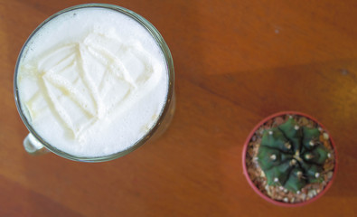 cream of hot coffee and cactus on wooden table, selective focus