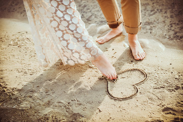 Couple legs paint heart on sand.