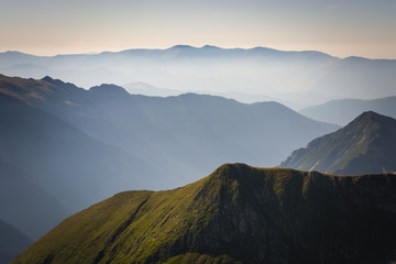 Naklejka na ściany i meble Fog in the mountains, three mountain ranges with a blue sky on the horizon