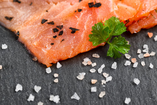 Smoked wild salmon slices with seasoning herbs on natural black